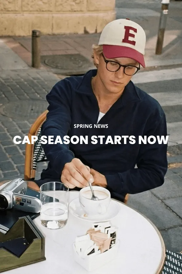 Een man zit op een houten kist in een studio en draagt een klassieke bruine cowboyhoed van vilt met brede rand, een donker denim overhemd en een spijkerbroek.